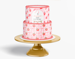 Two-tiered pink baby shower cake with strawberry pattern on a gold cake stand.