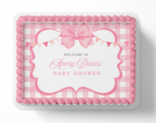 Pink baby shower cake with decorative elements and text on a white background
